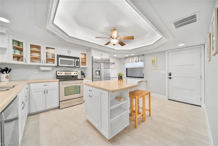 Kitchen with a breakfast bar area, a kitchen island, a raised ceiling, white cabinetry, and stainless steel appliances