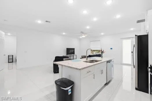 Kitchen featuring stainless steel appliances, white cabinetry, light tile patterned floors, sink, and an island with sink