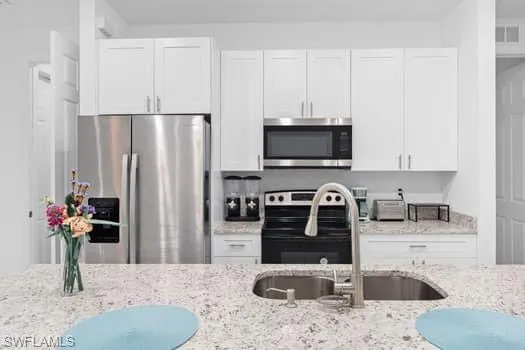 Kitchen featuring light stone countertops, sink, white cabinetry, and stainless steel appliances