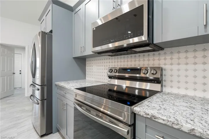 Kitchen with appliances with stainless steel finishes, tasteful backsplash, gray cabinets, and light stone countertops