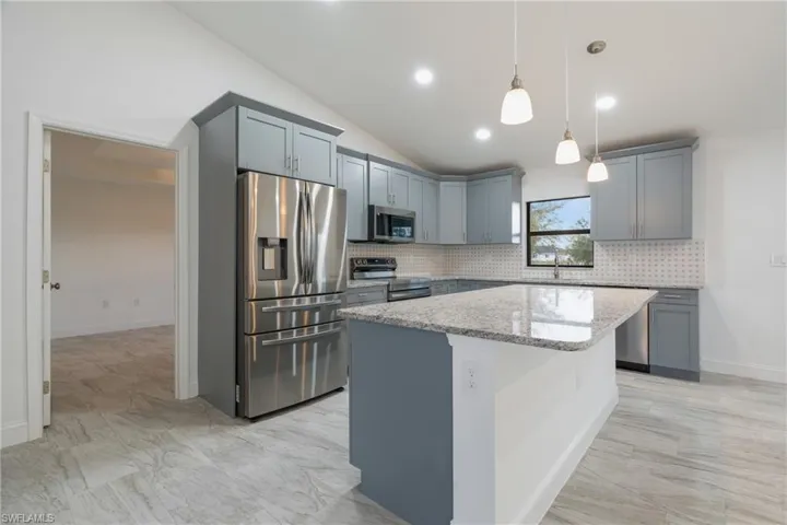 Kitchen with gray cabinets, appliances with stainless steel finishes, tasteful backsplash, vaulted ceiling, and recessed lighting