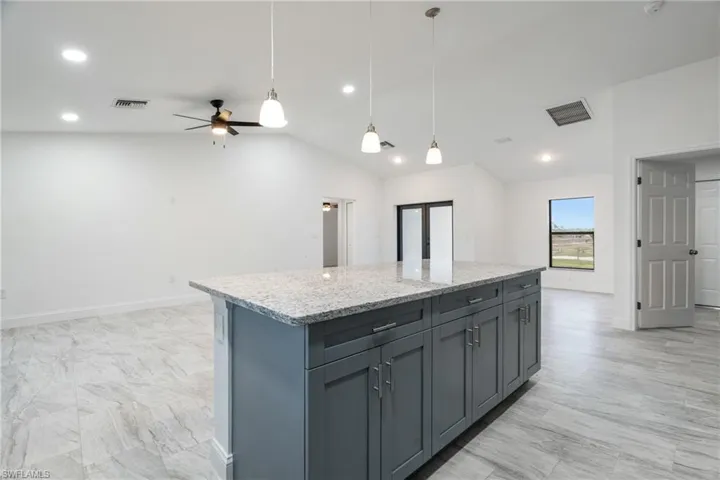 Kitchen with light stone countertops, pendant lighting, a kitchen island, lofted ceiling, and a ceiling fan