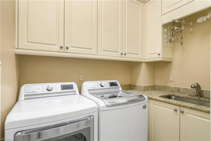 Utility room with washer and dryer, custom cabinetry and granite counter with laundry tub. Garment hanging space above tub.