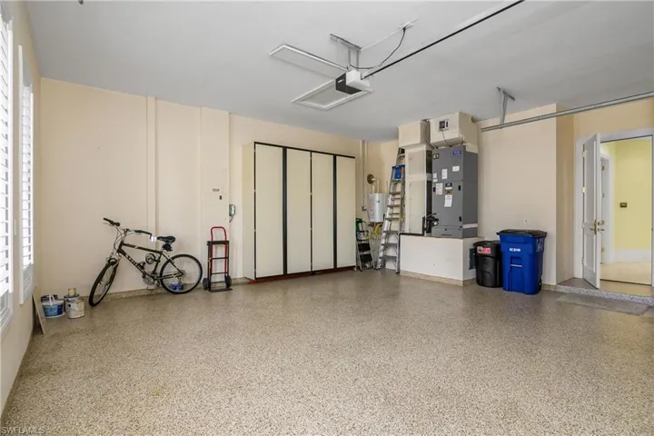 Two vehicle garage with epoxy flooring, custom cabinetry, tankless water heater, and air handler for one of the 2-zoned HVAC systems. Open door leads to utility room.