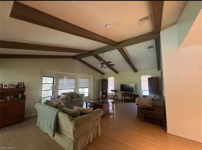 Living room with visible vents, baseboards, lofted ceiling with beams, light wood-style flooring, and ceiling fan