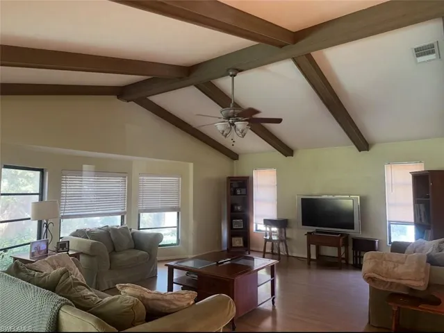 Living room featuring lofted ceiling with beams, dark wood-style flooring, visible vents, and a ceiling fan