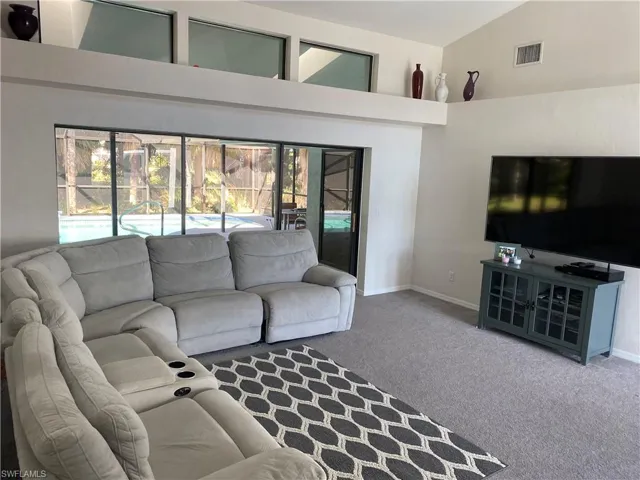 Living room with carpet floors, high vaulted ceiling, baseboards, and visible vents