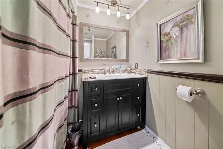 Bathroom with ornamental molding, a shower with curtain, vanity, wainscoting, and dark wood-type flooring