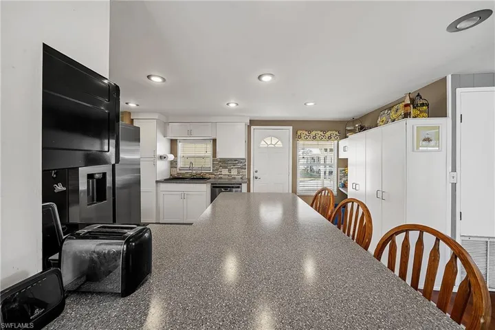 Kitchen with white cabinets, decorative backsplash, a breakfast bar area, recessed lighting, and stainless steel appliances