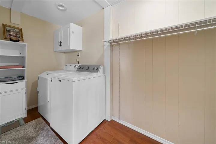 Laundry room featuring dark wood-style floors, washing machine and clothes dryer, and cabinet space