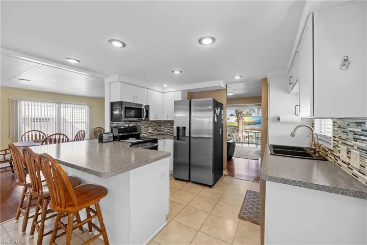 Kitchen with appliances with stainless steel finishes, backsplash, a peninsula, a breakfast bar area, and white cabinets