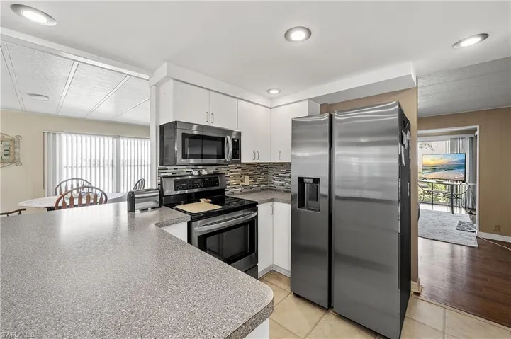 Kitchen featuring stainless steel appliances, white cabinets, wooden walls, tasteful backsplash, and light tile patterned flooring