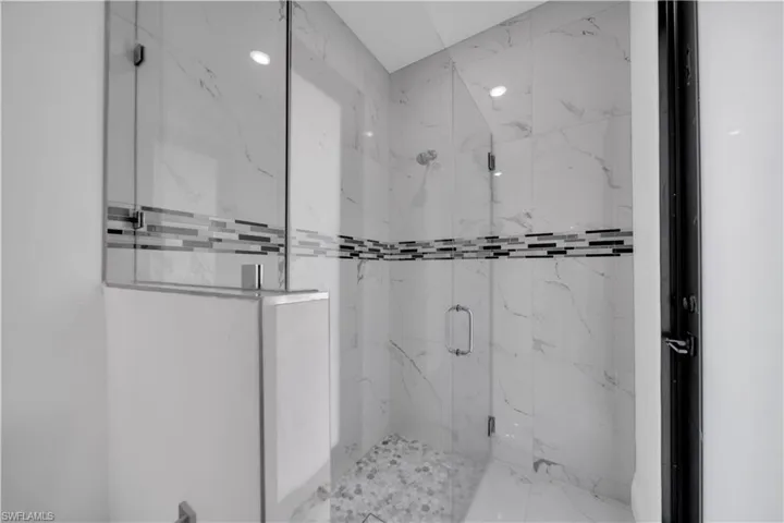 Glass-enclosed shower featuring large format wall tile with a linear mosaic accent, pebble-style floor, and ceiling-mounted recessed lighting