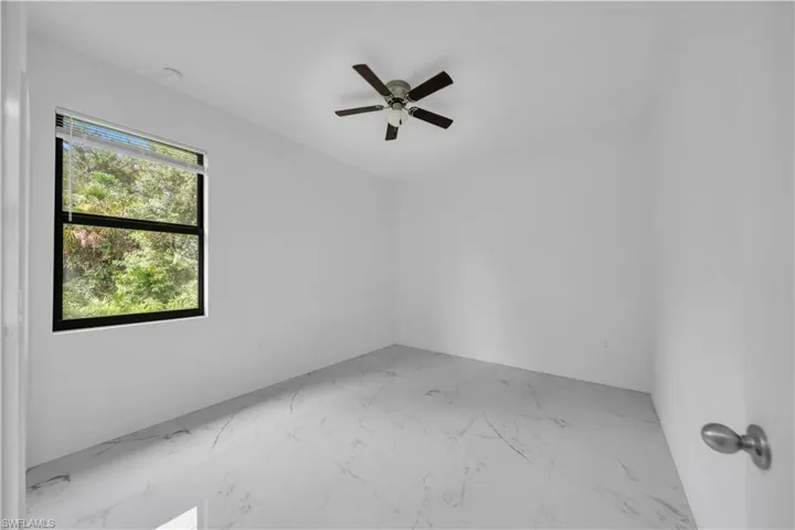 Bright room featuring white walls, large window, ceiling fan, and light-toned marble-look tile flooring