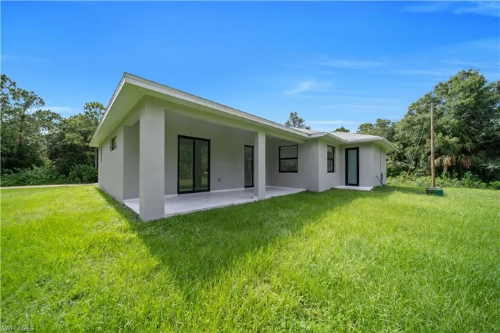 Expansive rear yard featuring a covered patio, multiple sliding glass door entries, and a private treed perimeter