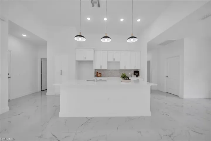 Open-concept kitchen featuring a large central island with a solid surface countertop, white cabinetry, a tiled backsplash, and recessed lighting