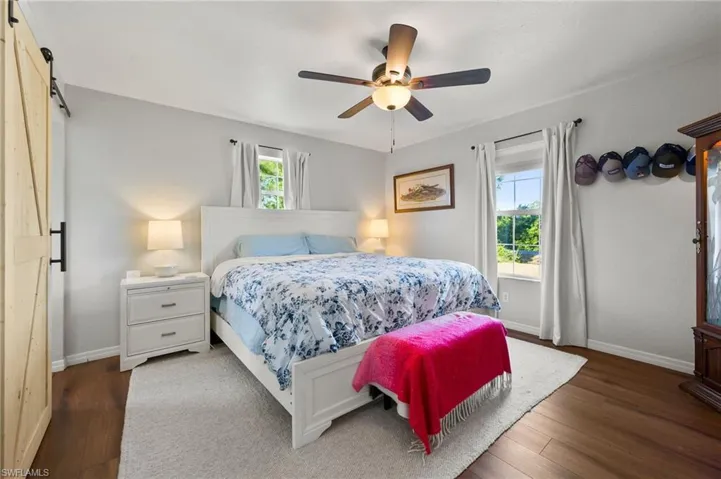 Bedroom with wood finished floors, ceiling fan, baseboards, and a barn door