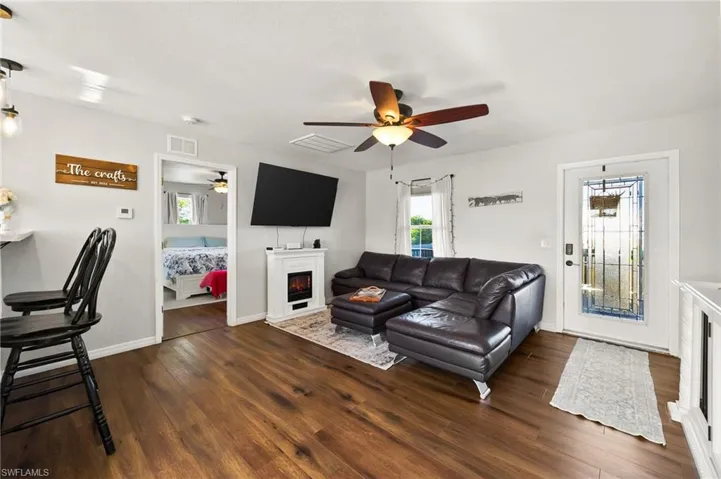Living room featuring dark wood-style floors, visible vents, a warm lit fireplace, and ceiling fan