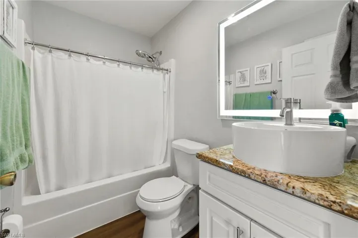 Bathroom featuring toilet, shower / bath combo, wood finished floors, and vanity