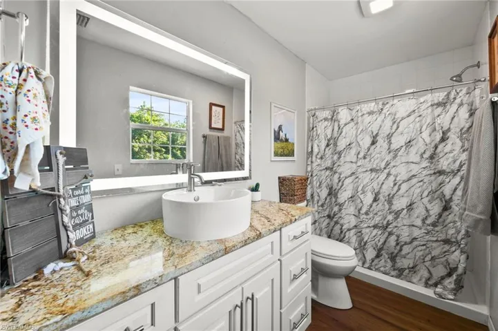Full bathroom featuring vanity, visible vents, toilet, curtained shower, and wood finished floors