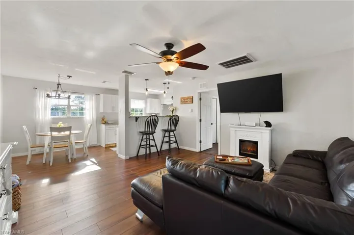 Living room with a glass covered fireplace, dark wood-type flooring, visible vents, and ceiling fan with notable chandelier