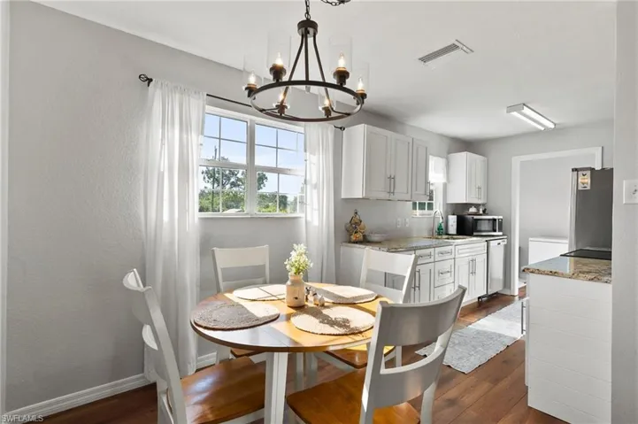 Dining space featuring an inviting chandelier, baseboards, visible vents, and dark wood-style flooring