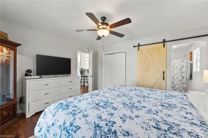 Bedroom featuring visible vents, baseboards, a barn door, dark wood-style flooring, and a ceiling fan