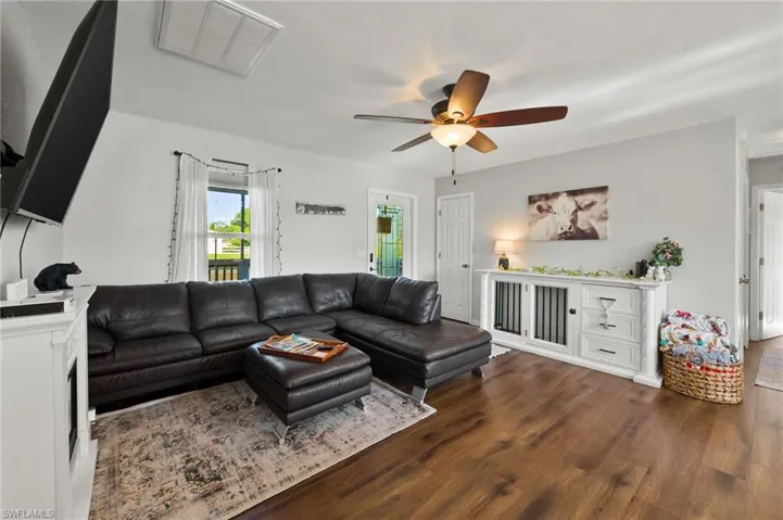 Living room featuring dark wood-style flooring, ceiling fan, and visible vents