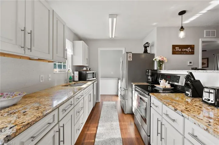 Kitchen with visible vents, wood finished floors, light stone counters, a sink, and stainless steel appliances