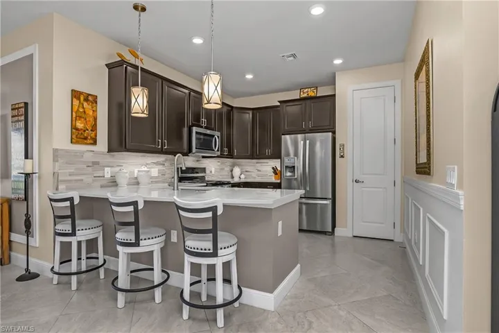 Kitchen with stainless steel appliances, pendant lighting, dark wood finish cabinetry, and a breakfast bar and pantry