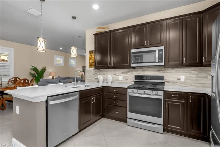 Kitchen featuring stainless steel appliances, a peninsula, dark wood finish cabinets, decorative light fixtures, and light stone counters