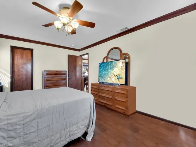 Bedroom with ceiling fan, crown molding, and dark wood-type flooring