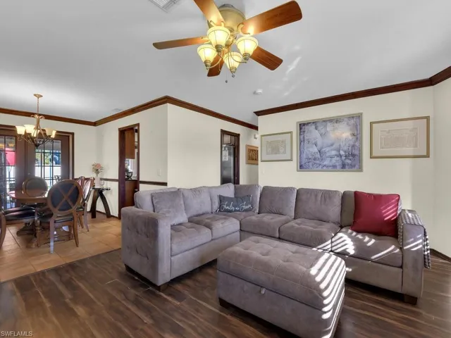 Living room featuring ceiling fan with notable chandelier, dark hardwood / wood-style flooring, and ornamental molding