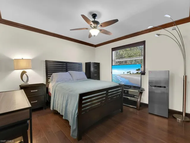 Bedroom featuring stainless steel fridge, dark hardwood / wood-style floors, ceiling fan, and ornamental molding
