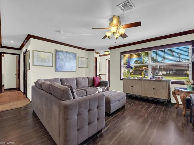 Living room featuring ornamental molding, ceiling fan, and dark wood-type flooring