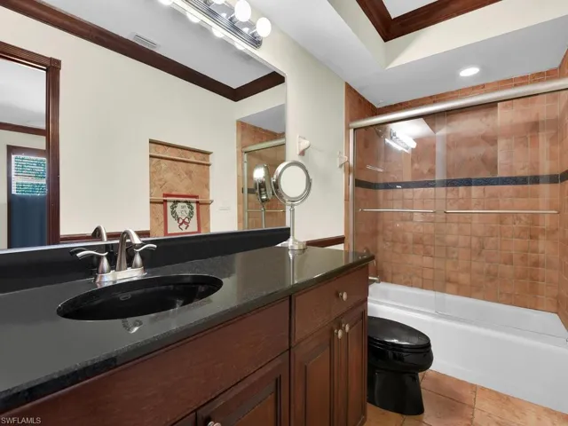 Full bathroom with vanity, bath / shower combo with glass door, crown molding, tile patterned flooring, and toilet