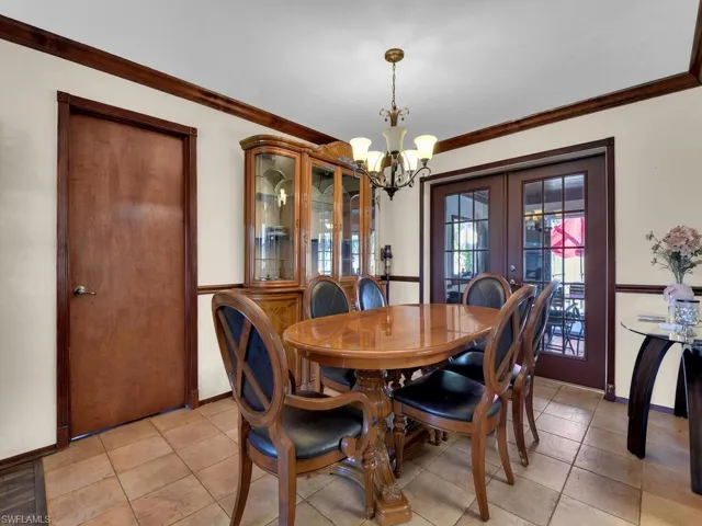 Tiled dining room featuring french doors, crown molding, and a notable chandelier