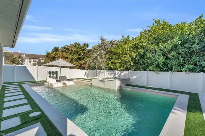 View of custom heated salt water swimming pool and sun deck featuring spa with overflow feature