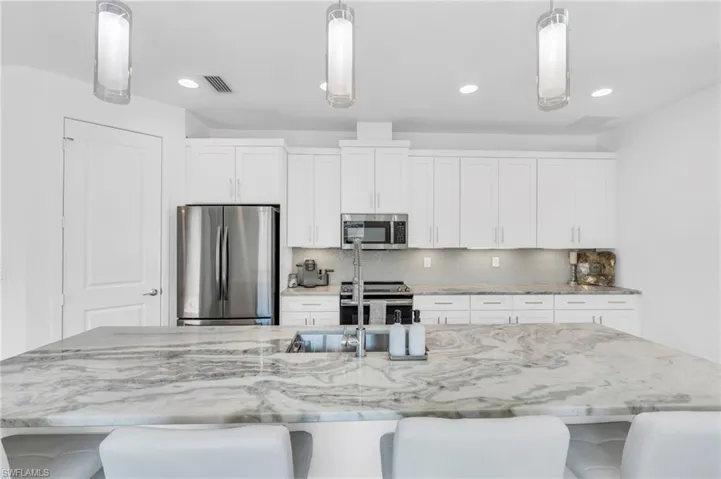 Kitchen featuring stainless steel appliances and a very large island, hanging light fixtures, and white cabinets
