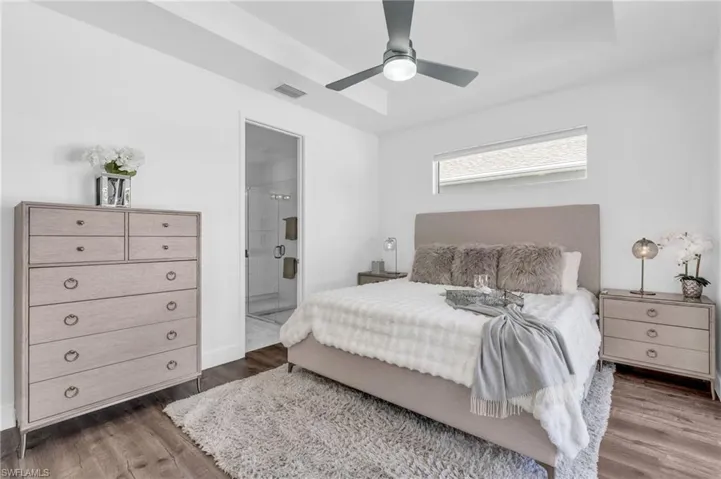 Bedroom with ceiling fan, ensuite bathroom, dark hardwood / wood-style flooring, and a raised ceiling