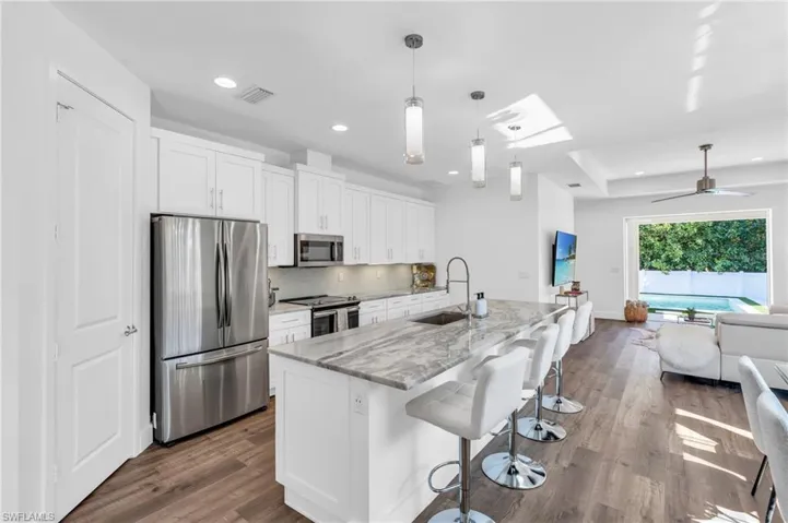 Kitchen featuring in island sink, appliances with stainless steel finishes, white cabinetry, light stone countertops, all pull out cabinetry in every cabinet!
