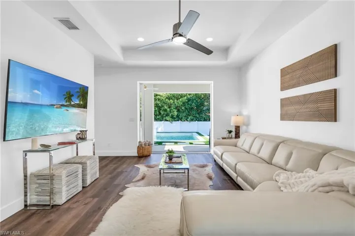 Living room featuring dark hardwood / wood-style floors, ceiling fan, and a tray ceiling with can lighting