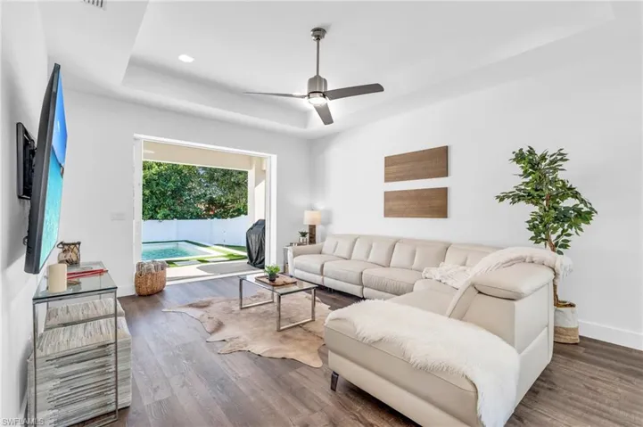 Living room featuring dark wood-type flooring, a raised ceiling, and ceiling fan