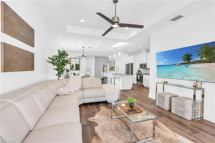 Living room with ceiling fan with notable chandelier, dark hardwood / wood-style flooring,