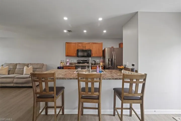 Kitchen featuring appliances with stainless steel finishes, light wood-style flooring, a kitchen bar, recessed lighting, and brown cabinetry