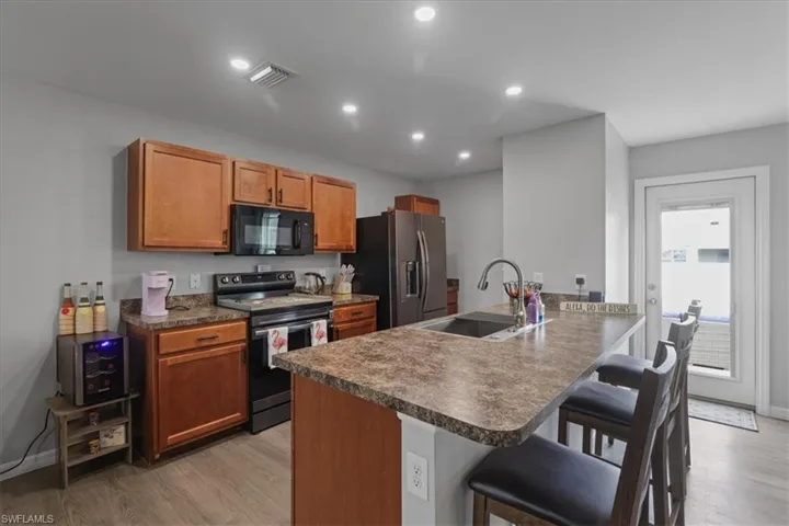 Kitchen featuring stainless steel appliances, a breakfast bar area, light wood-type flooring, a peninsula, and dark countertops