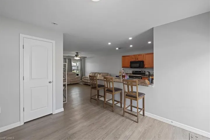 Kitchen featuring black appliances, a kitchen bar, brown cabinetry, light wood-style flooring, and recessed lighting