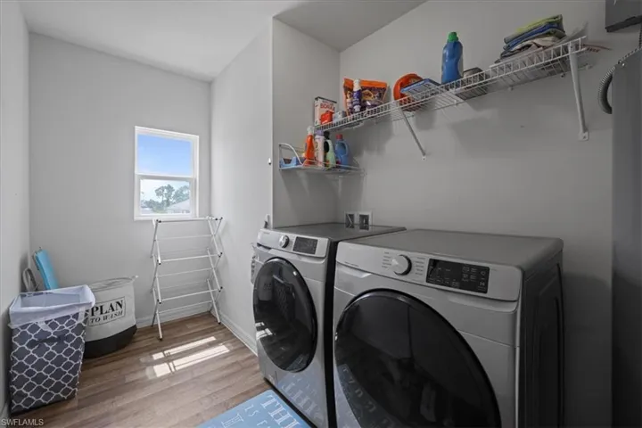 Washroom with washing machine and clothes dryer and light wood-style flooring