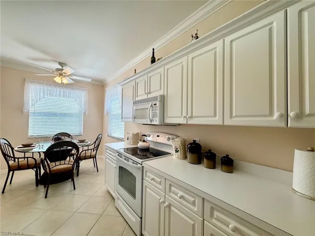 Kitchen with white appliances, crown molding, light countertops, white cabinets, and a ceiling fan