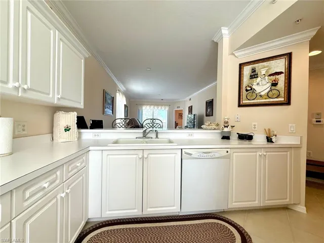 Kitchen with white cabinets, white dishwasher, ornamental molding, light countertops, and light tile patterned floors